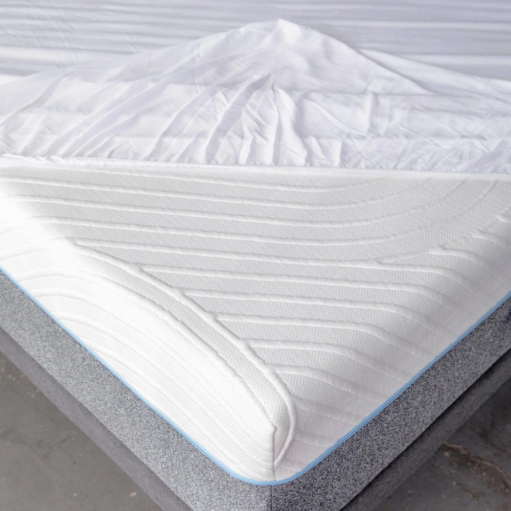 Close-up of a mattress protector with a gray base and white top on a plain background.