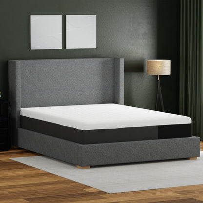 Gray upholstered bed with white mattress in a room with dark walls and a lamp.