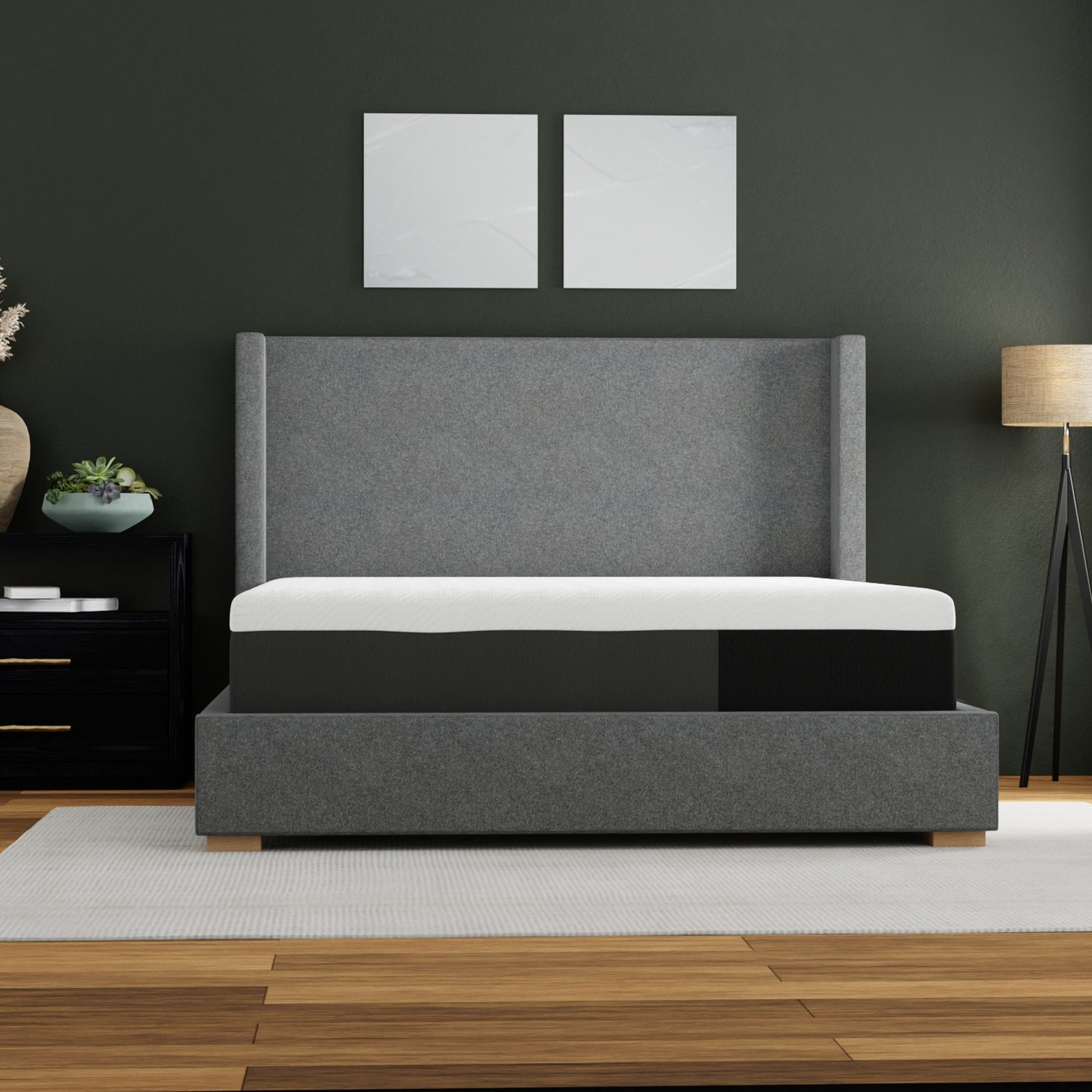 Gray upholstered bed with white mattress in a room with dark walls and wooden flooring.