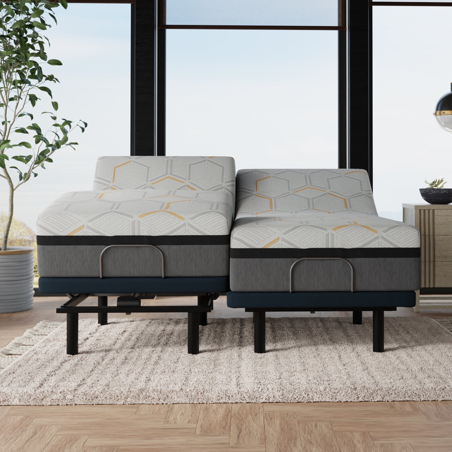 Gray adjustable bed with geometric pattern in a room with large windows and a plant. showing a split king set of mattresses with individual controls for each side of the bed.