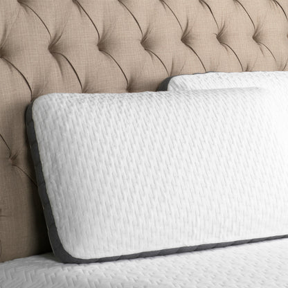 Two-Sided-bamboo-charcoal-Pillow with cool gel slab on one side, and plain charcoal infused memory foam on the other side. Pillow with white and gray cover leans on an upholstered headboard