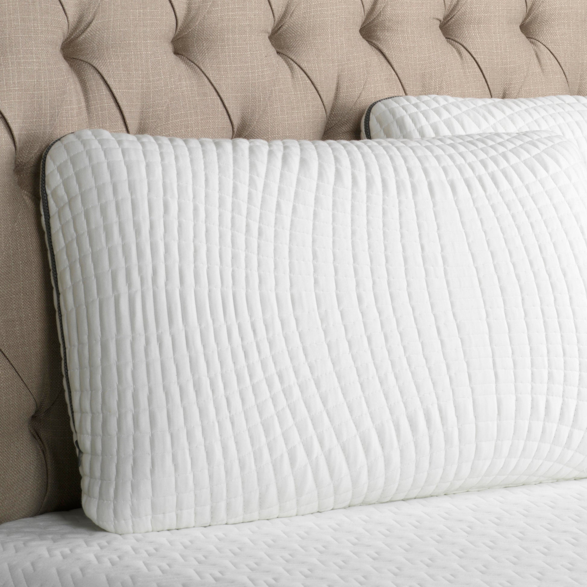 White pillow with a dark gray zipper. Bamboo Charcoal infused Pillow leaning on an upholstered headboard