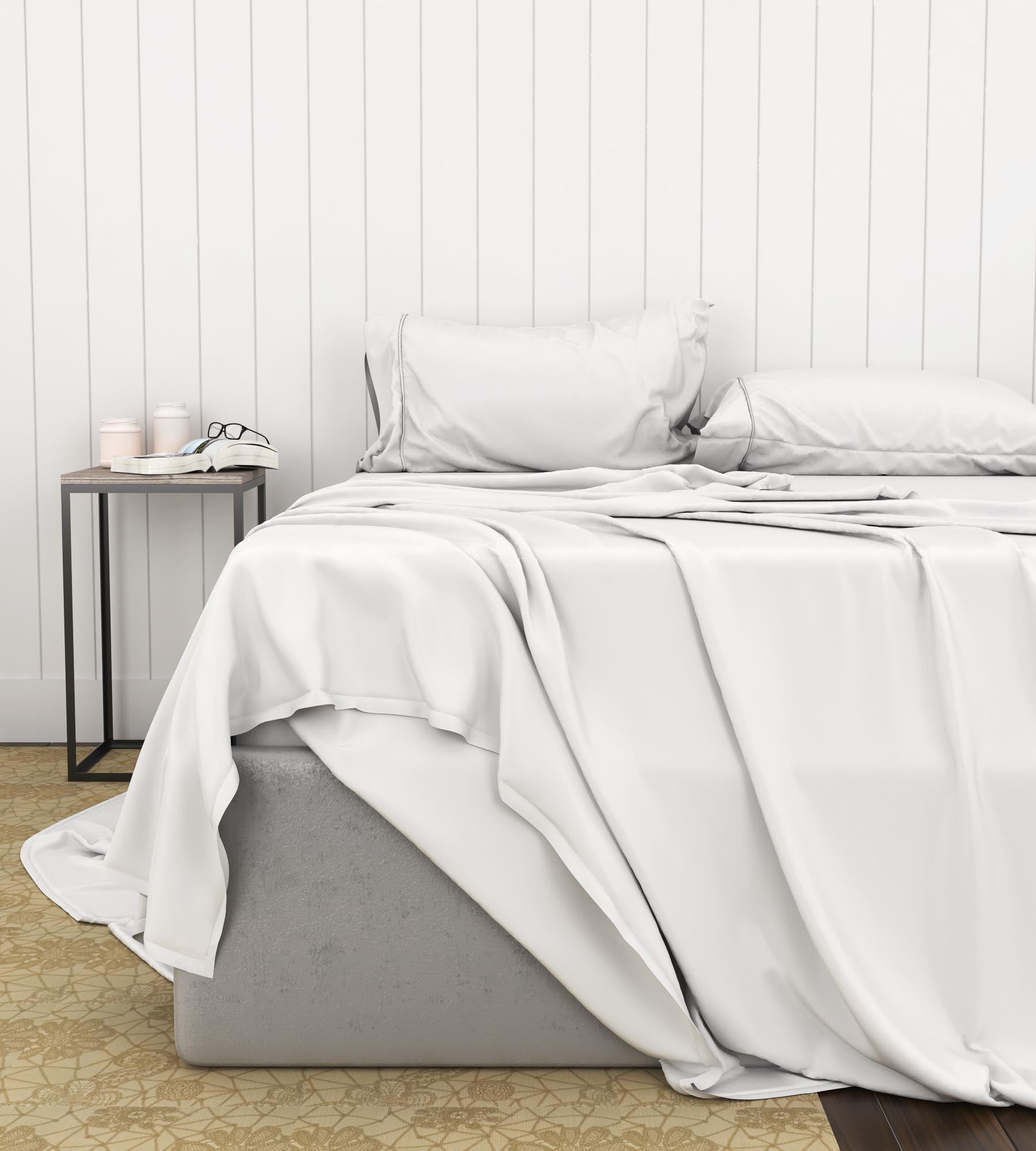 Neatly made bed with white luxury sheet set on a bed in a room with a wooden floor and white paneled walls.