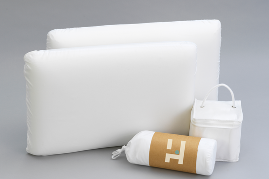 Two white pillows and a rolled-up mattress protector and Sheet set with an Owen Holmes branding on a gray background