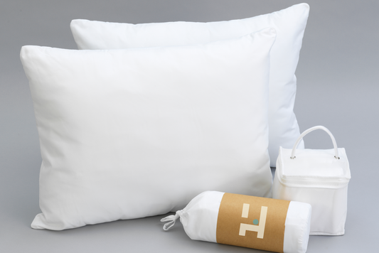 Two white pillows, a rolled-up mattress protector with an Owen Holmes logo, and a Sheet Set white on a gray background.