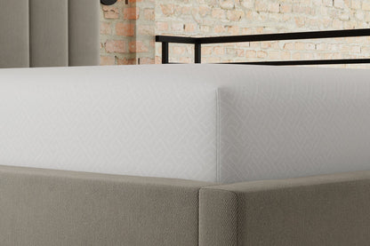 Close-up of a bed with a textured mattress protector and headboard against a brick wall.