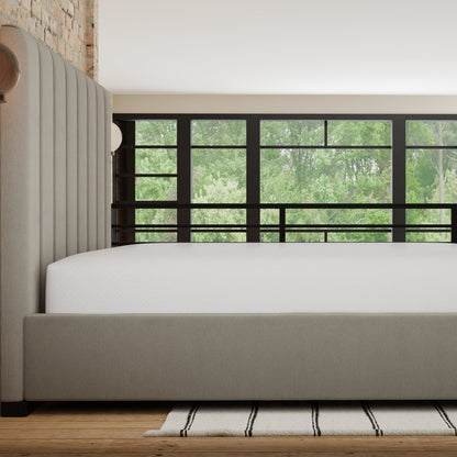 Beige bed in a room with large windows showing greenery outside. mattress is covered with the Fresh Mattress protector. viewed from the side