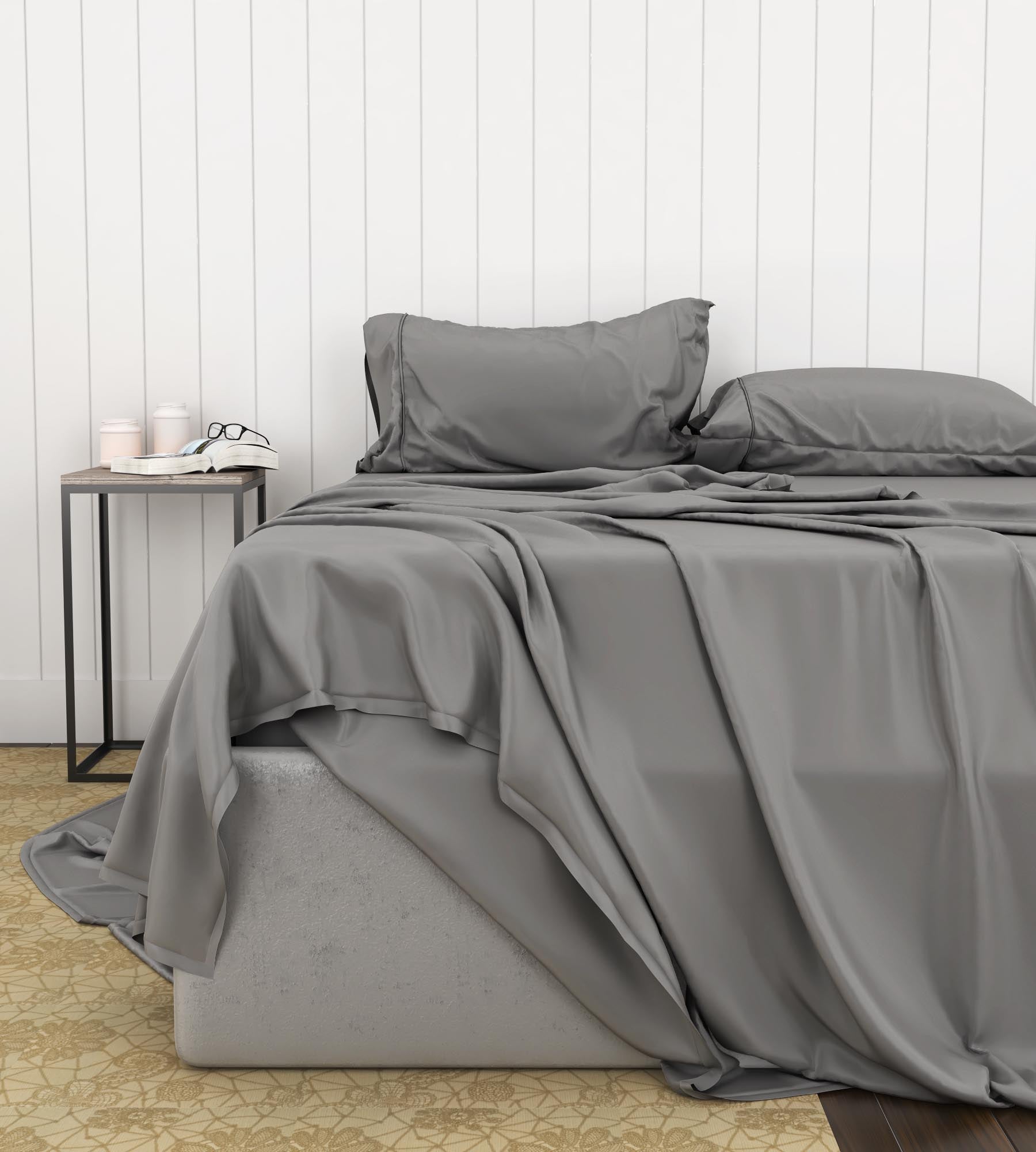 Gray sheet set on a bed with a white wooden panel wall in the background