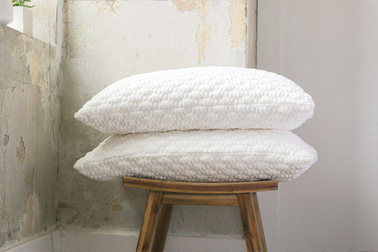 Two white pillows stacked on a wooden stool against a textured wall. Shredded memory foam pillows
