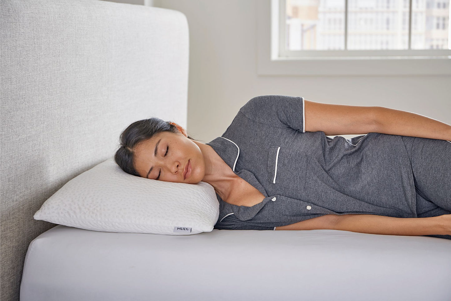 Woman sleeping on a bed / mattress with a cooling shredded memory foam pillow, wearing a gray outfit.