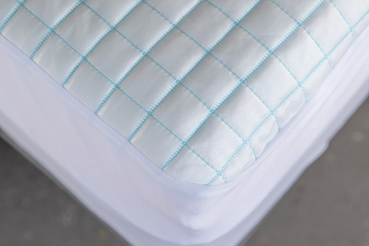 Close-up of a white mattress protector with light blue grid pattern. Shows cooling feature