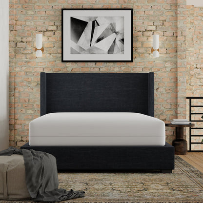 Modern bedroom with a black upholstered bed against a brick wall. Mattress has Igloo-Mattress_encasement_protector