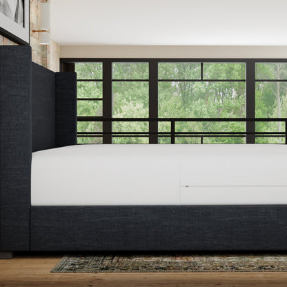 Modern bedroom with a bed and large window showing greenery outside. mattress has a waterproof mattress encasement on it- side view