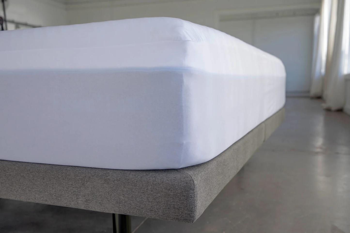 Mattress protector on a queen-size mattress on a bed frame with a neutral background