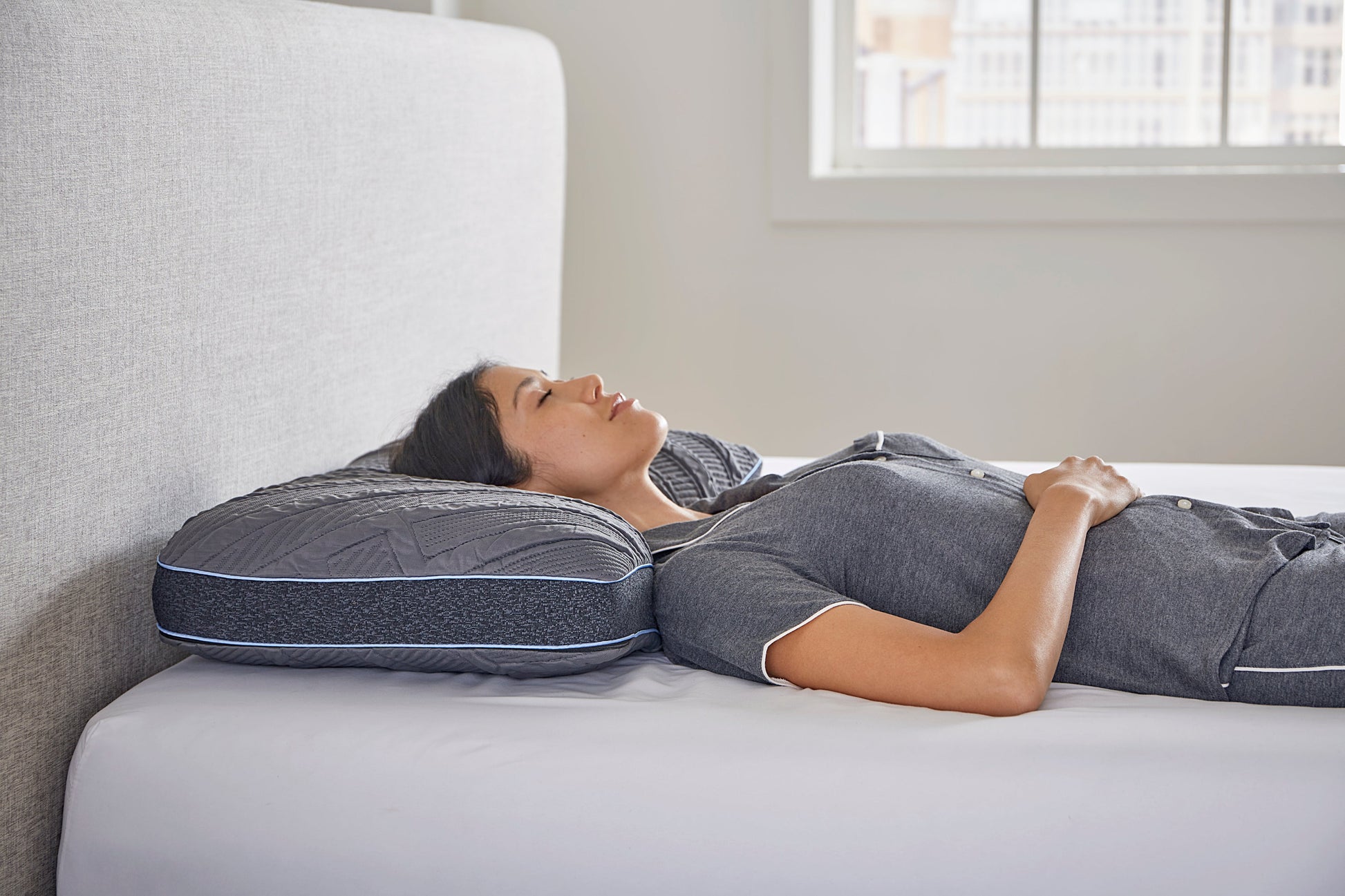 Person lying on a mattress with a comfortable cooling pillow, in a bedroom setting.