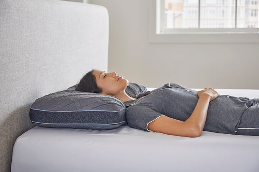 Person lying on a mattress with a comfortable cooling pillow, in a bedroom setting.