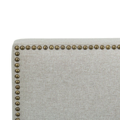 Close-up of a light gray upholstered bed with brass nailhead trim on a white background