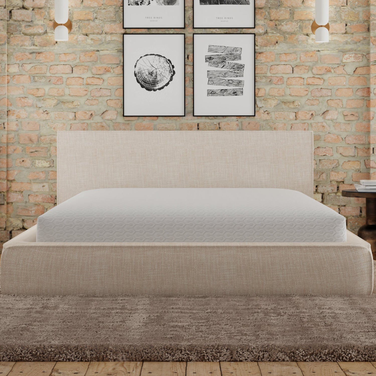 upholstered Bed with a mattress covered with Snow mattress protector. Bed is against a brick wall with framed artwork.