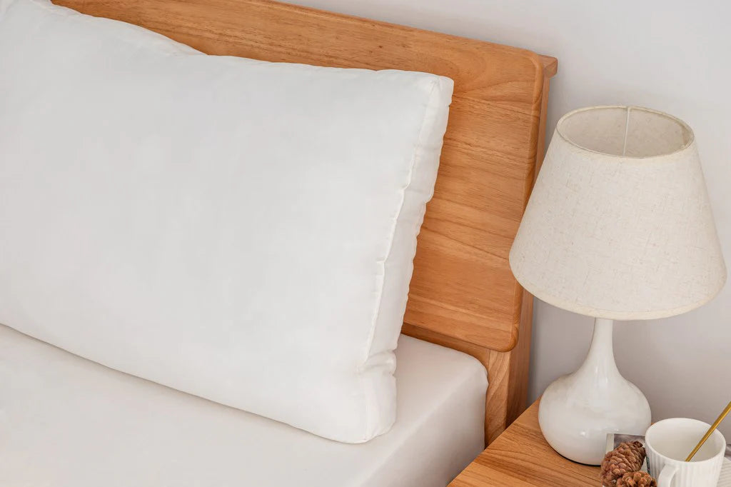 Soft washed down alternative pillow on a wooden bed frame with a bedside lamp, showcasing plush loft and smooth cover.