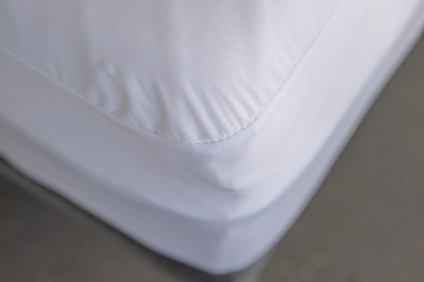 Close-up of a white mattress protector on a bed with a gray blurred background
