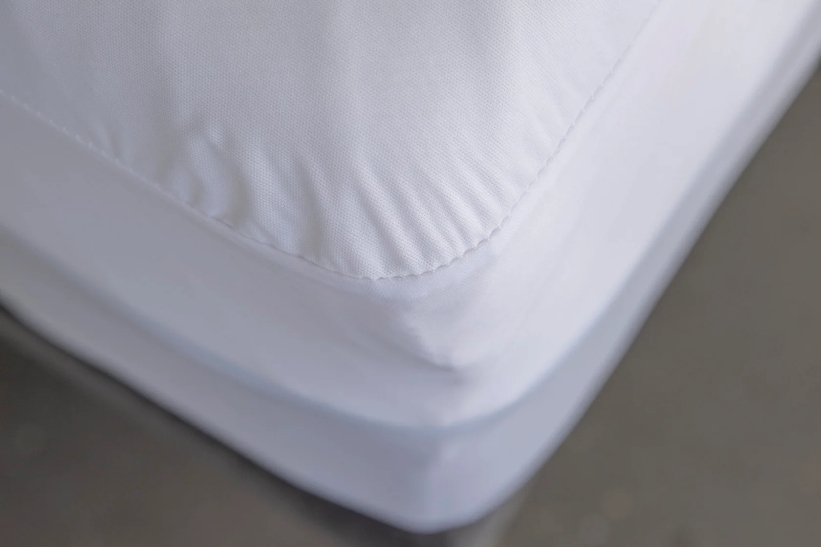 Close-up of a white mattress protector on a bed with a gray blurred background