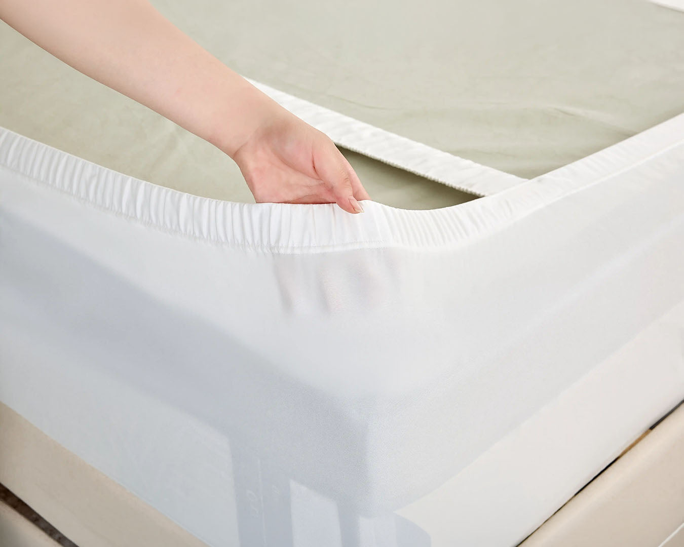 A close-up of a white fitted mattress Protector being pulled over a mattress by a person's hand