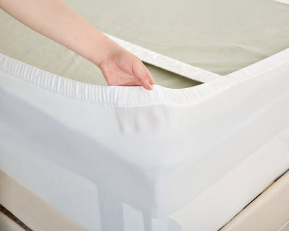 A close-up of a white fitted mattress Protector being pulled over a mattress by a person's hand