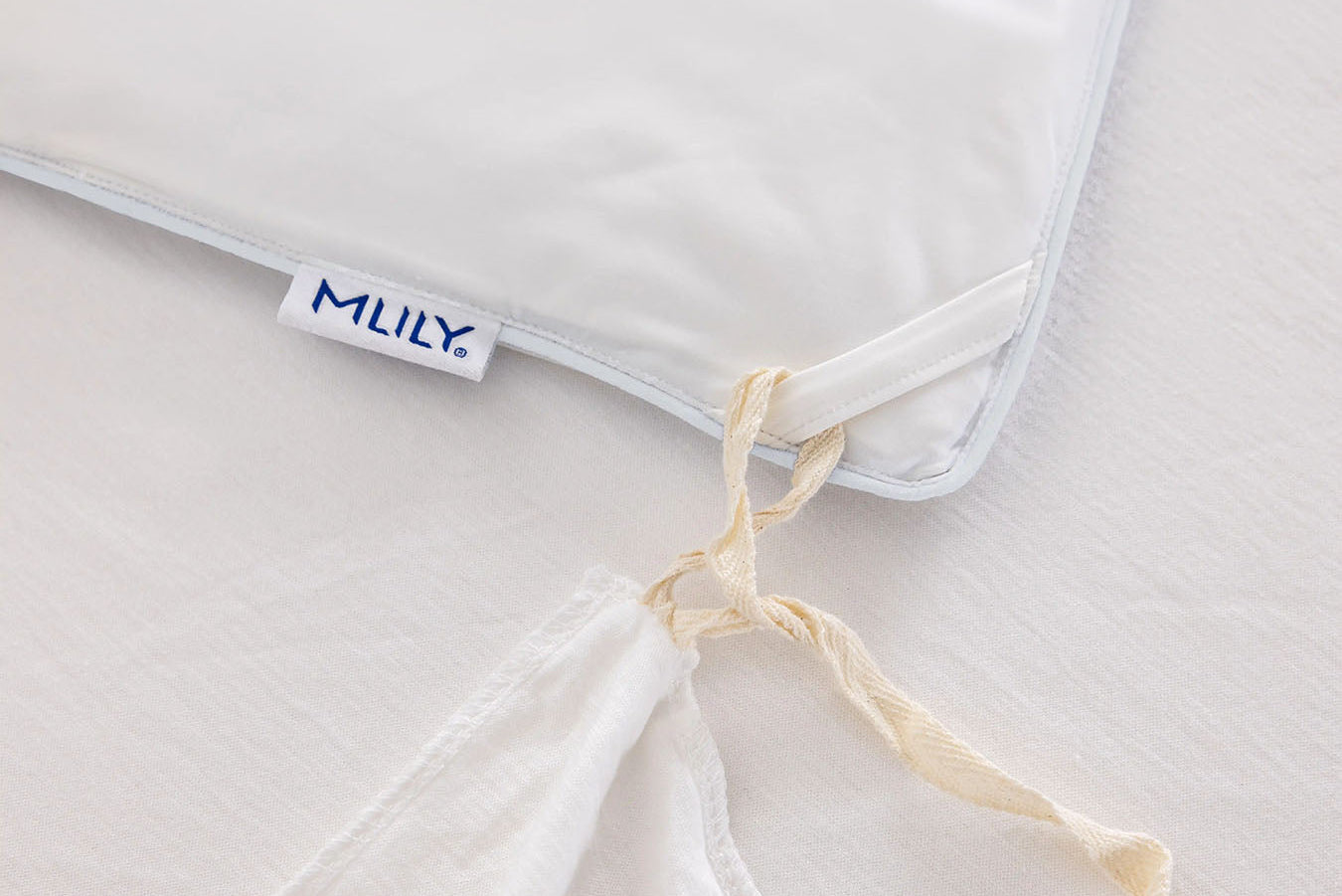 Close-up of a white cooling duvet insert with a visible Mlily brand tag, tied with a cream-colored string on a matching white duvet surface.