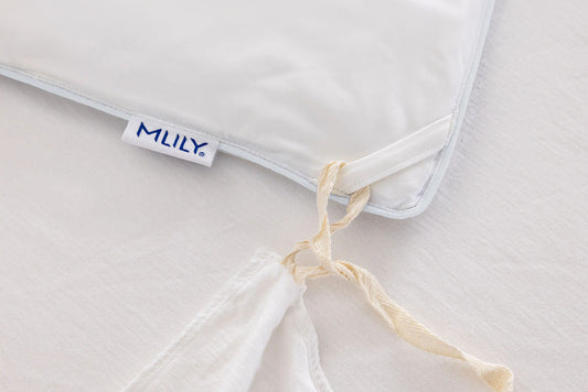 Close-up of a white cooling duvet insert with a visible Mlily brand tag, tied with a cream-colored string on a matching white duvet surface.
